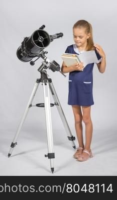 Schoolgirl leafing through a textbook while standing at the telescope