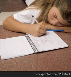 Schoolgirl lying on the floor and writing in a spiral notebook
