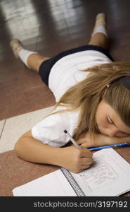 Schoolgirl lying on the floor and writing in a spiral notebook