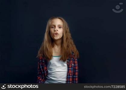 Schoolgirl makes face leaning against the glass in studio. Happy childhood, children having fun, funny kid isolated on dark background, child emotion. Schoolgirl makes face leaning against the glass