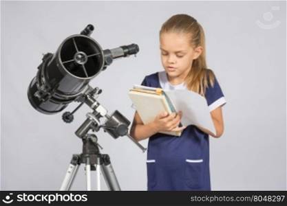 Schoolgirl reading a textbook while standing astronomer at the telescope