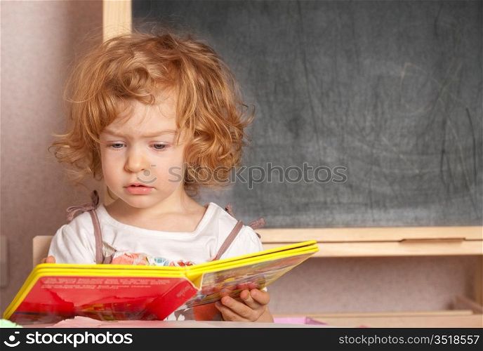 Schoolgirl reading textbook in a class against blackboard