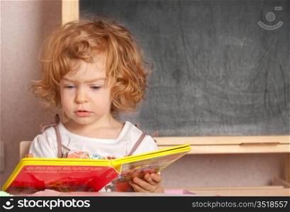 Schoolgirl reading textbook in a class against blackboard