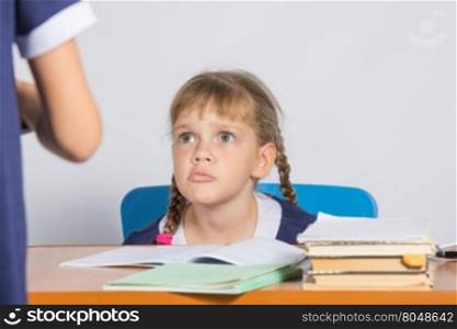 Schoolgirl sitting at the desk angrily looks at another girl