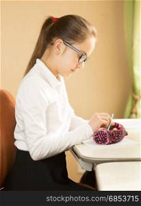Schoolgirl sitting behind table and taking pencil out of pencil case