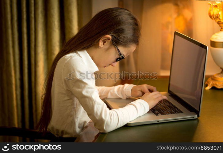 Schoolgirl sitting behind table and using laptop at cabinet