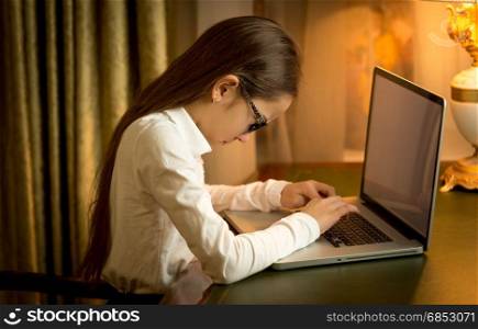 Schoolgirl sitting behind table and using laptop at cabinet