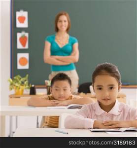 Schoolgirl sitting in a classroom with a schoolboy and a female teacher in the background