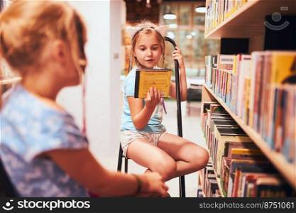 Schoolgirls looking for audio books in school library. Students choosing books. Elementary education. Doing homework. Learning from books. Back to school