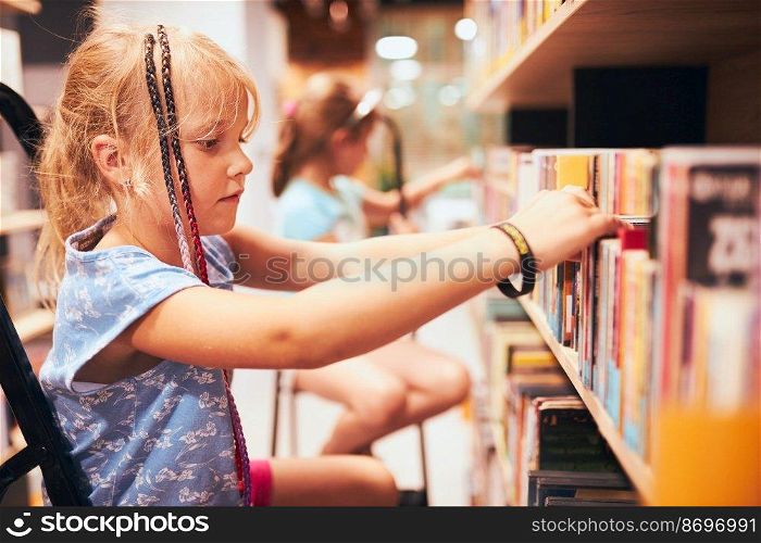 Schoolgirls looking for books in school library. Students choosing books. Elementary education. Doing homework. Learning from books. Back to school