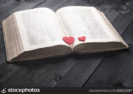 Schooling theme image with an antique open book and two red hearts on its pages, displayed on a vintage wooden table. A concept for reading, studying or romance.