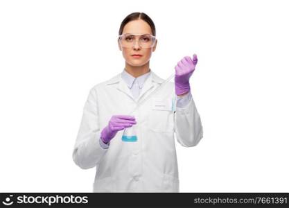 science, chemistry and people concept - young female scientist in goggles with pipette chemical in flask making test or research. female scientist in goggles with chemical in flask