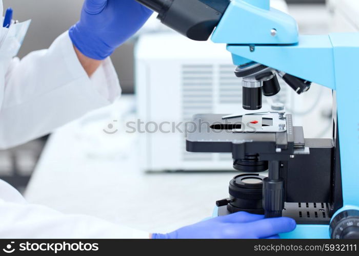 science, chemistry, biology, medicine and people concept - close up of scientist hands with microscope and blood test sample making research in clinical laboratory