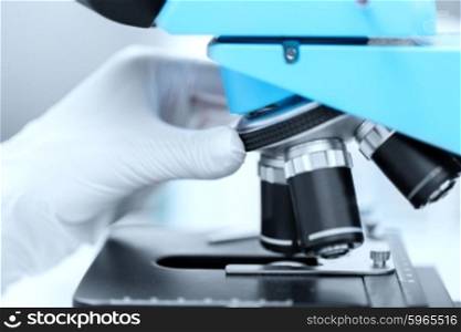 science, chemistry, biology, medicine and people concept - close up of scientist hand in glove setting microscope and making research in clinical laboratory
