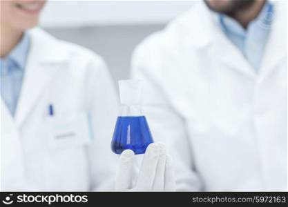science, chemistry, biology, medicine and people concept - close up of scientists with test tube or glass flask making test or research in clinical laboratory