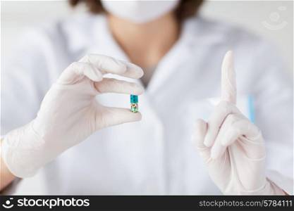 science, chemistry, biology, medicine and people concept - close up of young female scientist or doctor holding pill and pointing finger up in laboratory
