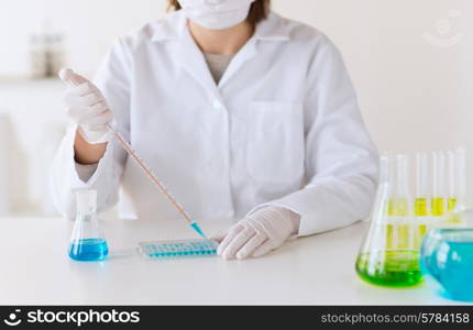 science, chemistry, biology, medicine and people concept - close up of young female scientist with pipette and flask making test or research in clinical laboratory