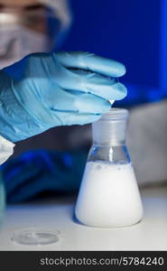 science, chemistry, biology, medicine and people concept - close up of young female scientist pouring chemical powder into flask making test or research in clinical laboratory