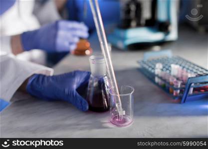 science, chemistry, biology, medicine and people concept - close up of young scientists with pipette and flasks making test or research in clinical laboratory