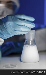 science, chemistry, biology, medicine and people concept - close up of young female scientist pouring chemical powder into flask making test or research in clinical laboratory