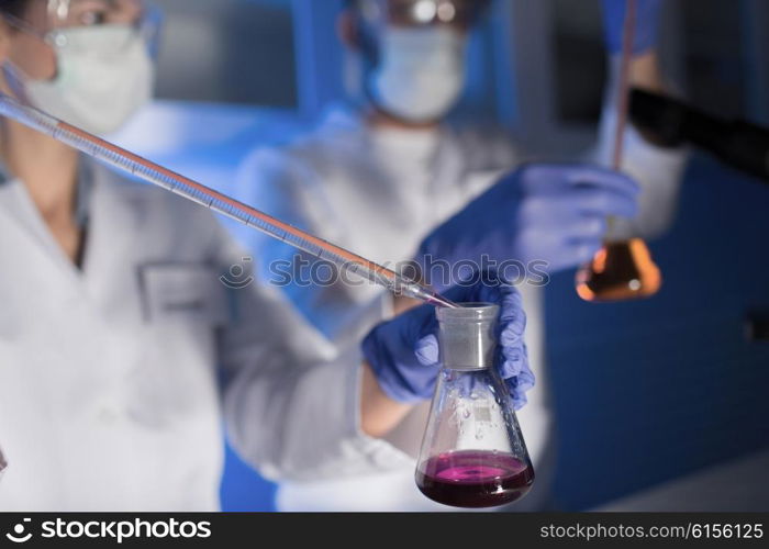 science, chemistry, biology, medicine and people concept - close up of young scientists with pipette and flasks making test or research in clinical laboratory