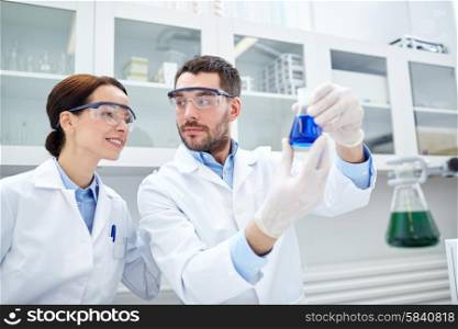 science, chemistry, biology, pharmacy and people concept - young scientists with pipette and flask making test or research in clinical laboratory