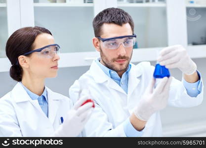 science, chemistry, biology, pharmacy and people concept - young scientists with pipette and flask making test or research in clinical laboratory