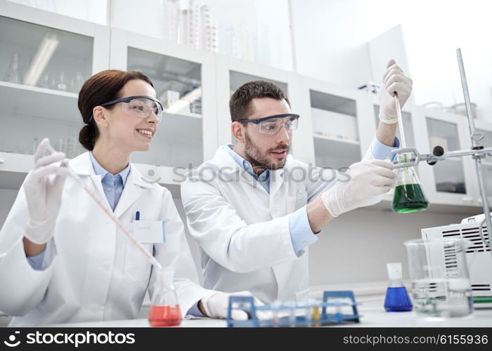 science, chemistry, biology, pharmacy and people concept - young scientists with pipette and flask making test or research in clinical laboratory