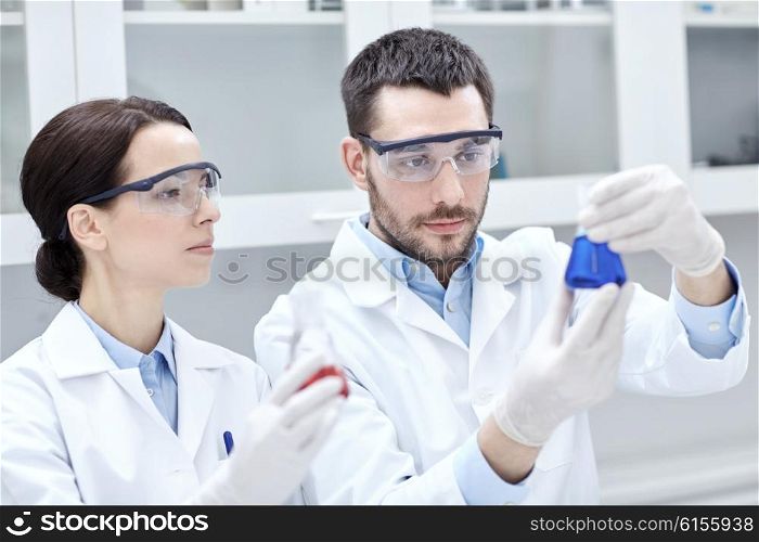 science, chemistry, biology, pharmacy and people concept - young scientists with pipette and flask making test or research in clinical laboratory