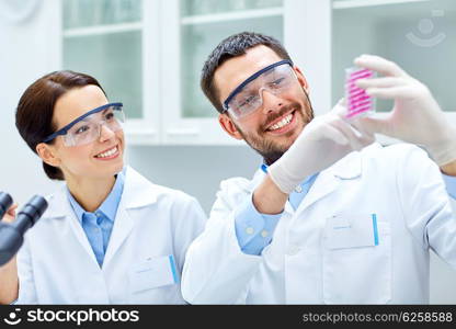 science, chemistry, biology, pharmacy and people concept - young scientists with pipette and flask making test or research in clinical laboratory