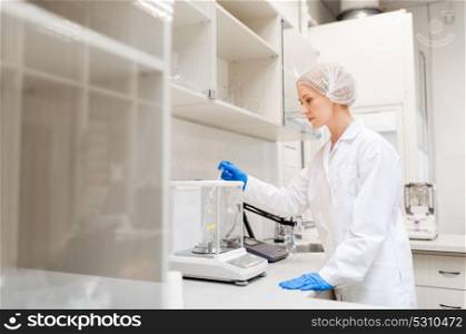 science, chemistry, industry and people concept - woman scientist or chemist adding sulphuric acid into flask on scale at laboratory. woman with sulphuric acid and scale at laboratory