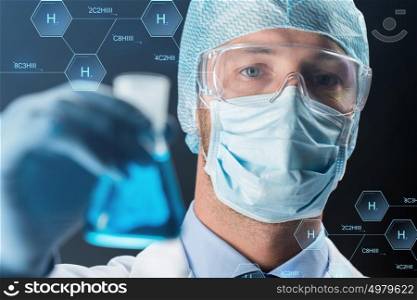 science, chemistry, research and people concept - close up of young scientist in protective mask, hat and goggles holding test flask with chemical over black background. close up of scientist holding flask with chemical