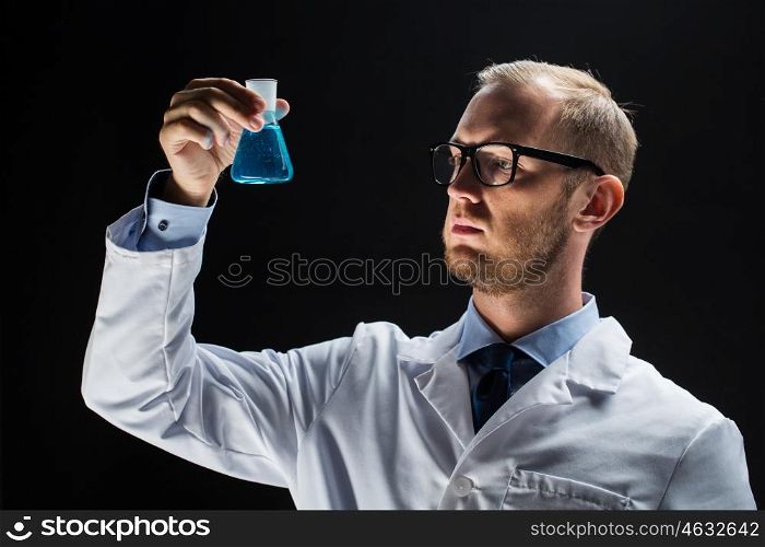 science, chemistry, research and people concept - young scientist holding test flask with chemical over black background