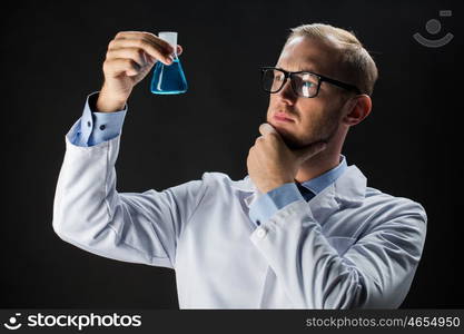 science, chemistry, research and people concept - young scientist holding test flask with chemical over black background