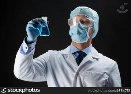 science, chemistry, research and people concept - young scientist in protective mask, hat and goggles holding test flask with chemical over black background