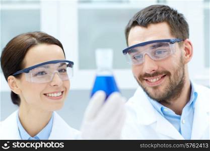 science, chemistry, research, biology and people concept - young scientists holding flask with medicine or chemical in clinical laboratory