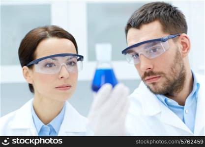 science, chemistry, research, biology and people concept - young scientists holding flask with medicine or chemical in clinical laboratory