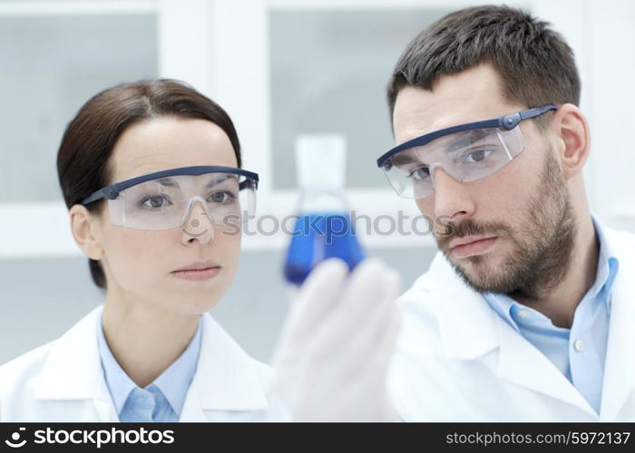 science, chemistry, research, biology and people concept - young scientists holding flask with medicine or chemical in clinical laboratory