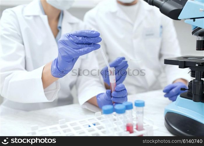 science, chemistry, technology, biology and people concept - close up of scientists hands with pipette and test tube making research in clinical laboratory
