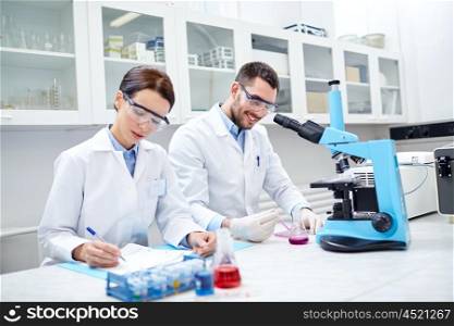 science, chemistry, technology, biology and people concept - young scientists shaking glass with reagent and making test or research in clinical laboratory