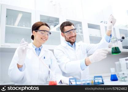 science, chemistry, technology, biology and people concept - young scientists with pipette and flask making test or research in clinical laboratory