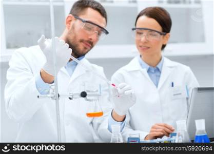 science, chemistry, technology, biology and people concept - young scientists with pipette and glass making test or research in clinical laboratory