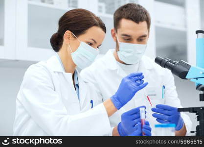 science, chemistry, technology, biology and people concept - young scientists with pipette and test tube making research in clinical laboratory