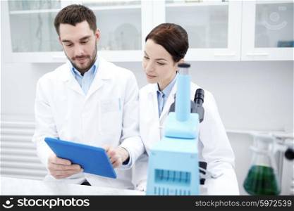 science, chemistry, technology, biology and people concept - young scientists with tablet pc and microscope making test or research in clinical laboratory