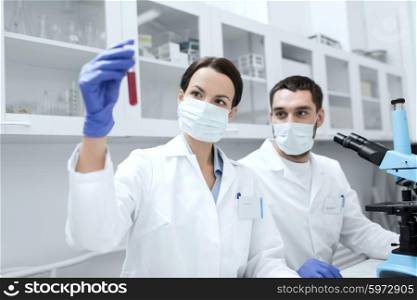 science, chemistry, technology, biology and people concept - young scientists with test tube and microscope making research in clinical laboratory