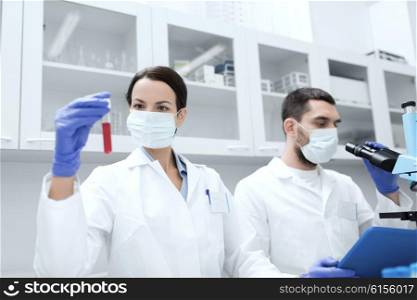 science, chemistry, technology, biology and people concept - young scientists with test tube and microscope making research in clinical laboratory
