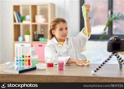 science, childhood and blogging concept - happy smiling little girl blogger with slime and camera on tripod recording video blog at home laboratory. girl with slime and camera video blogging at home