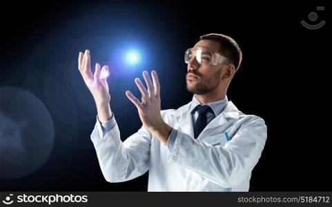 science, future technology and people concept - male doctor or scientist in white lab coat and safety glasses with light over black background. scientist in lab coat and goggles with light