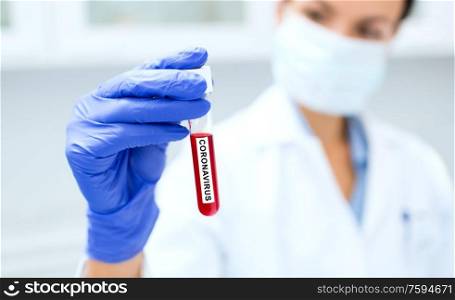 science, medicine and virus concept - close up of young female scientist holding test tube with blood sample for coronavirus research at clinical laboratory. scientist holding test tube with coronavirus