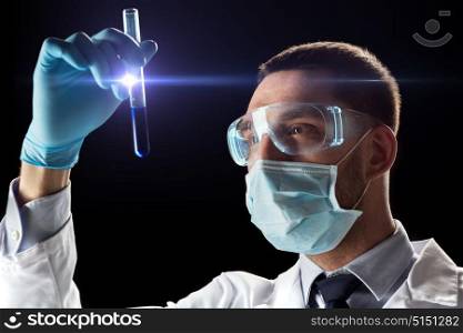 science, research and people concept - young scientist in safety glasses and face mask with test tube. scientist with safety glasses, mask and test tube